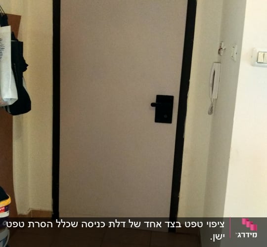 דלת עם מסגרת שחורה, ידית שחורה ודלי צבע על הרצפה